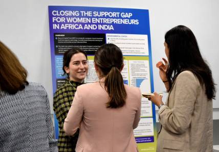 one student smiling in front of a poster talking to two other students